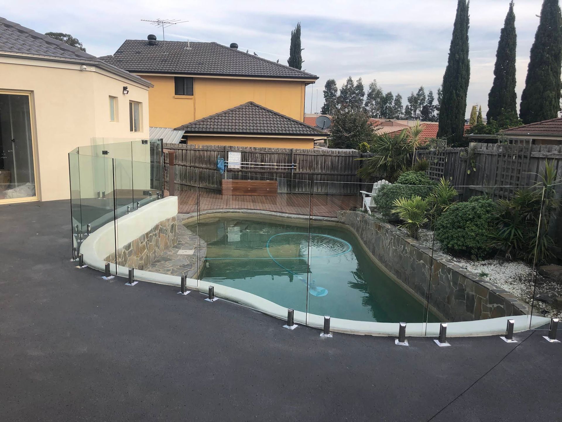 Backyard Pool With Green Water Beside a House and Patio — ClearView Glass Pool Fencing In Roselands, NSW