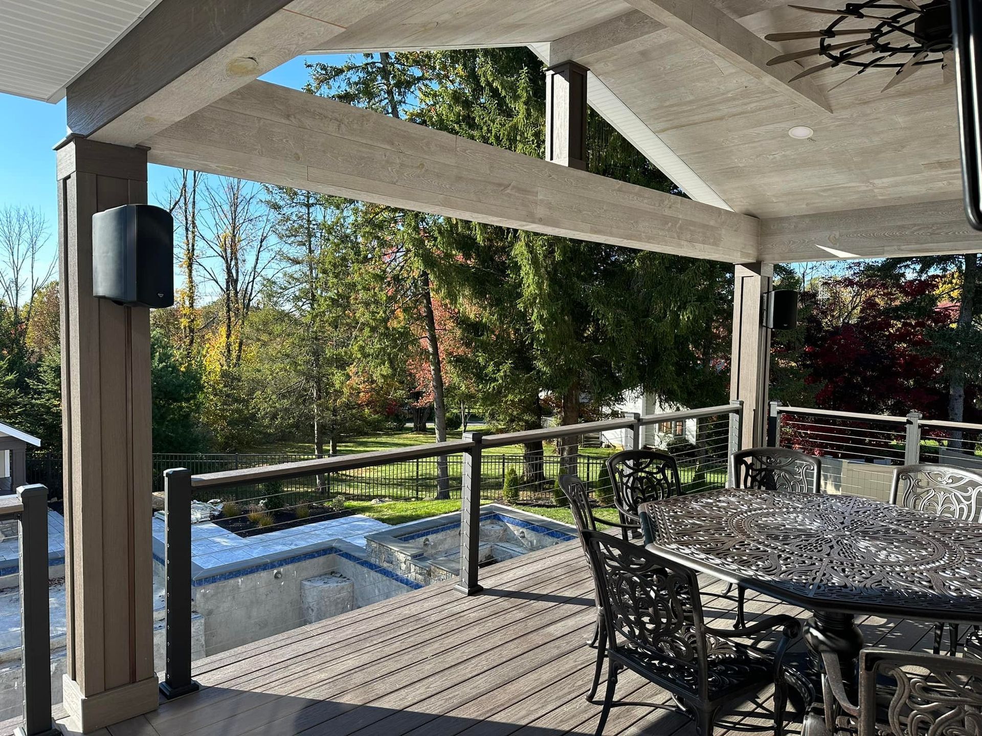 Outdoor deck with dining set, overlooking a grassy yard. Brown support beams and railings frame the view of trees.