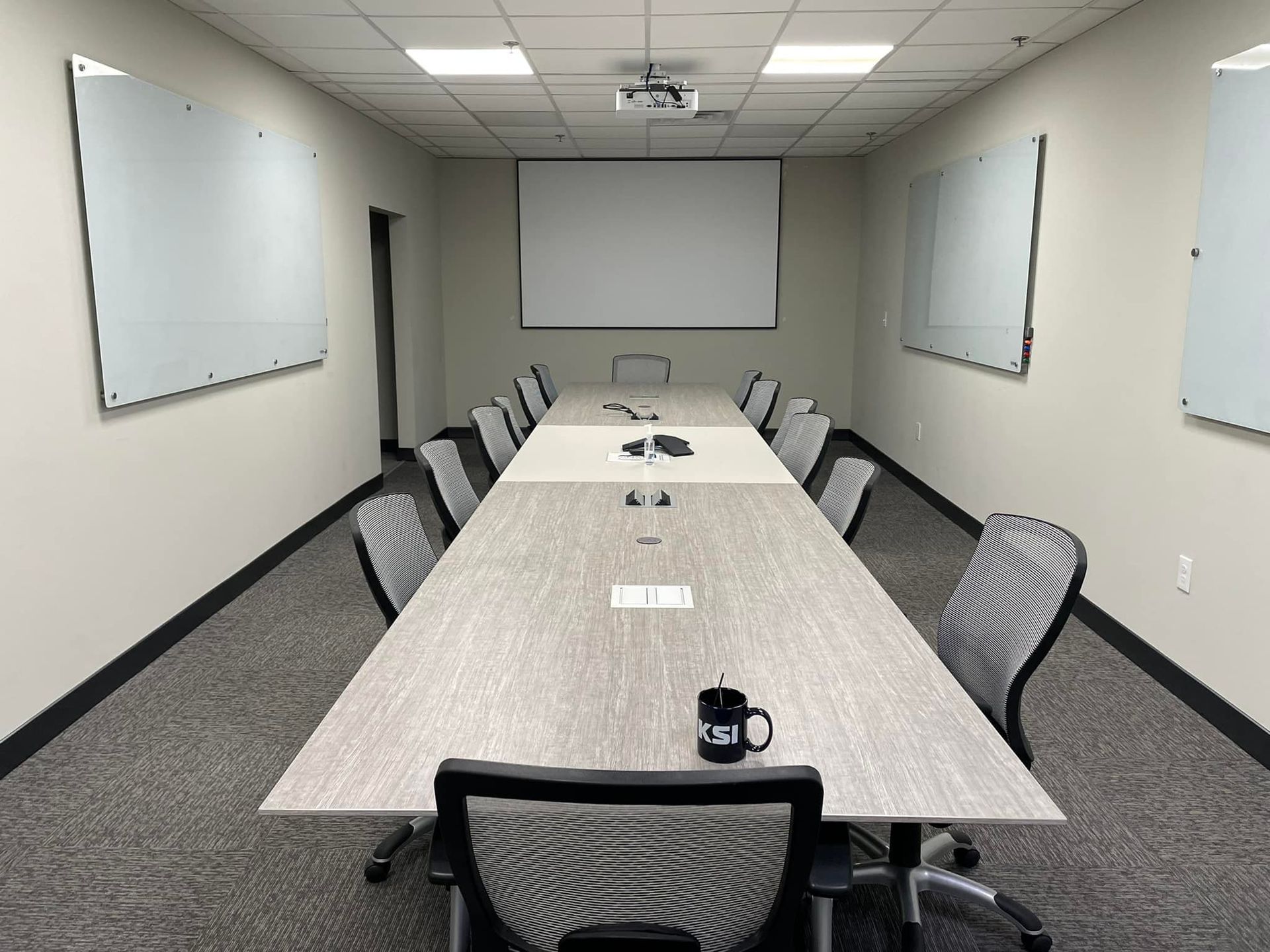 Conference room with long table, chairs, whiteboards, projection screen, and overhead projector.
