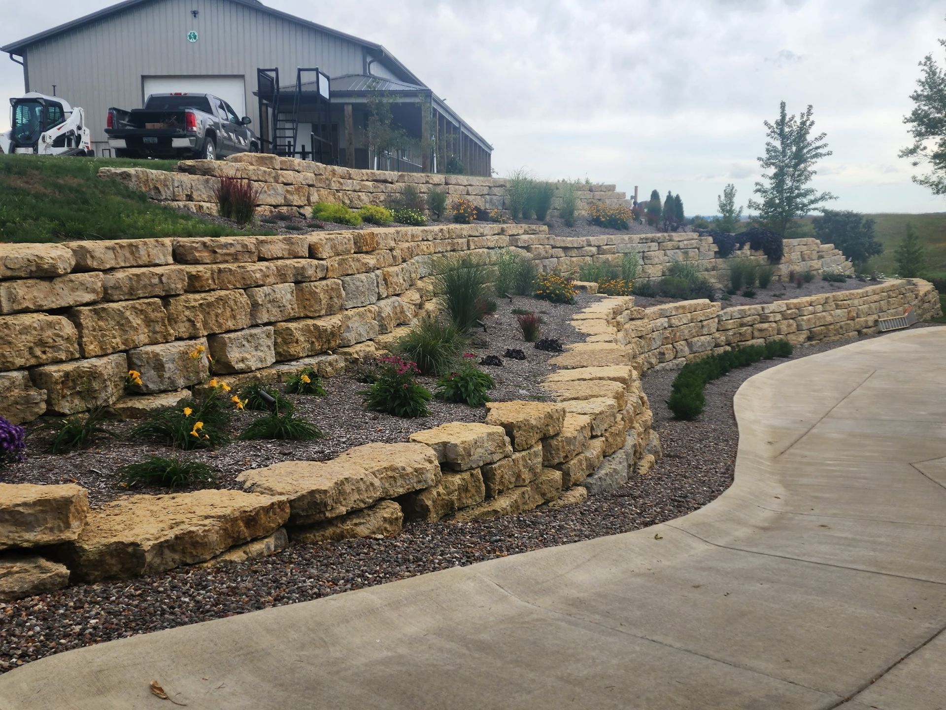 A large stone wall surrounds a driveway in front of a house.