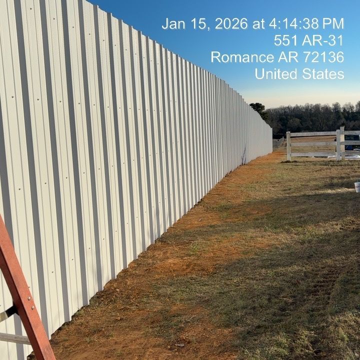 Long white corrugated fence along a grassy dirt lot under a blue sky.