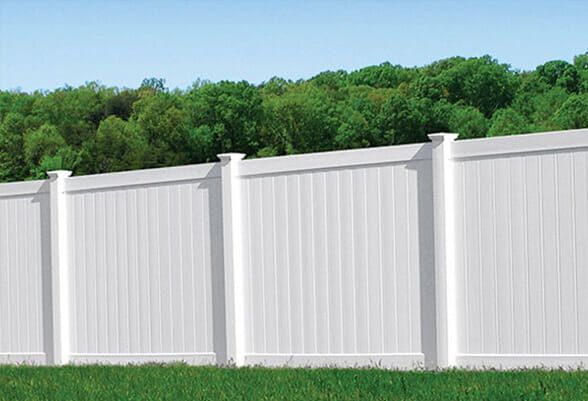 White vinyl privacy fence in front of green trees and grass under a clear blue sky