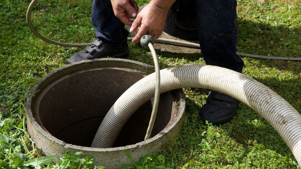 Worker pulling a white hose from an open manhole in the grass