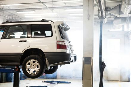White SUV on a lift in an auto repair shop with bright light and exhaust equipment nearby