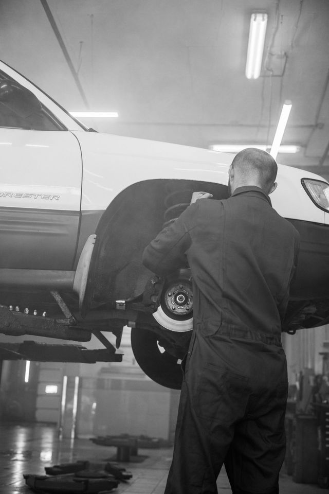 Mechanic inspecting underside of a white SUV on a lift in a garage