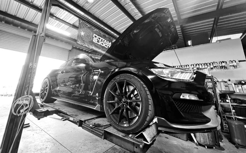 Black sports car on a lift in an auto shop with hood open, viewed from low angle