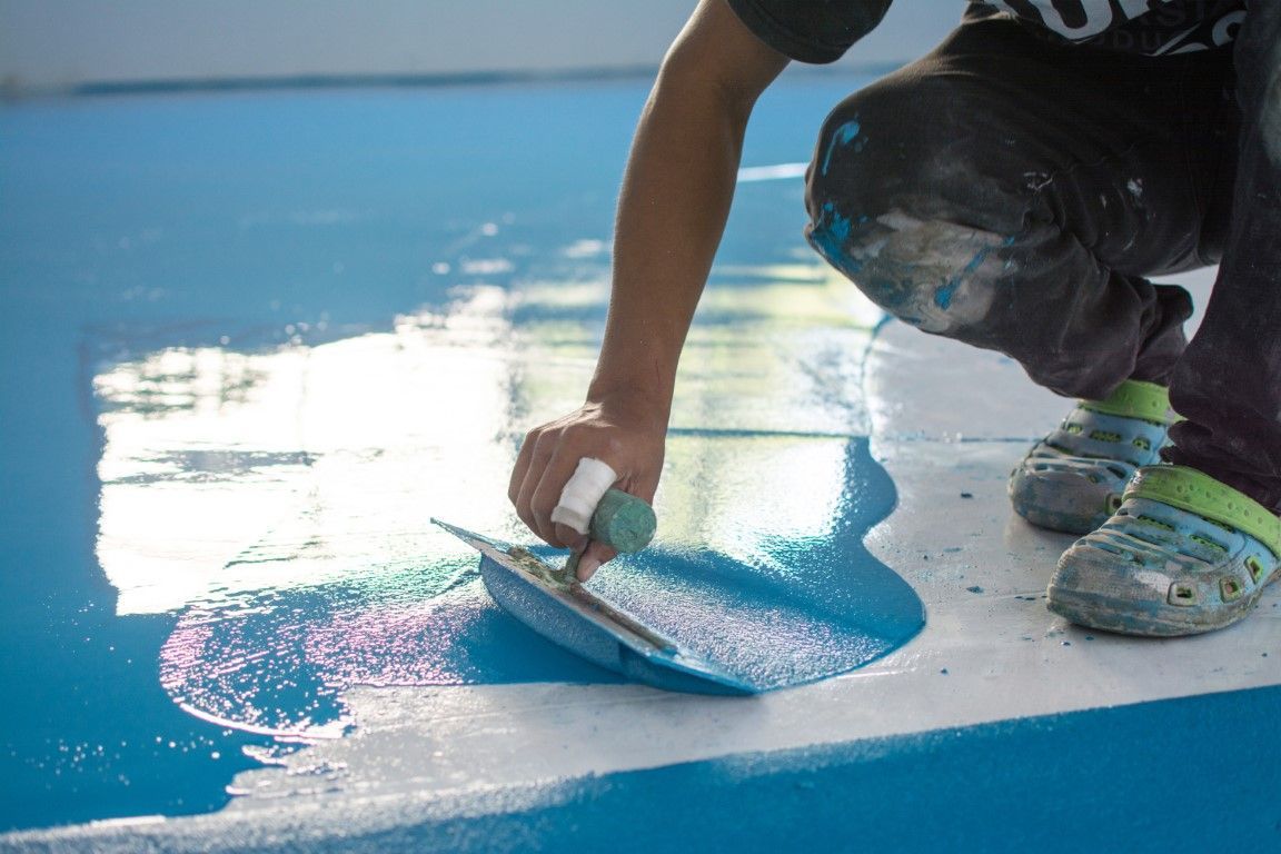 Worker applying blue epoxy floor coating with a squeegee in Kyle, TX