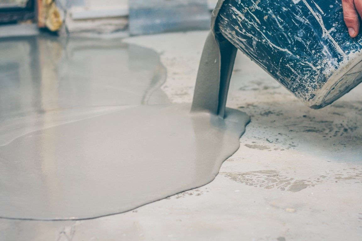 Worker pouring concrete floor coating material onto a prepped slab