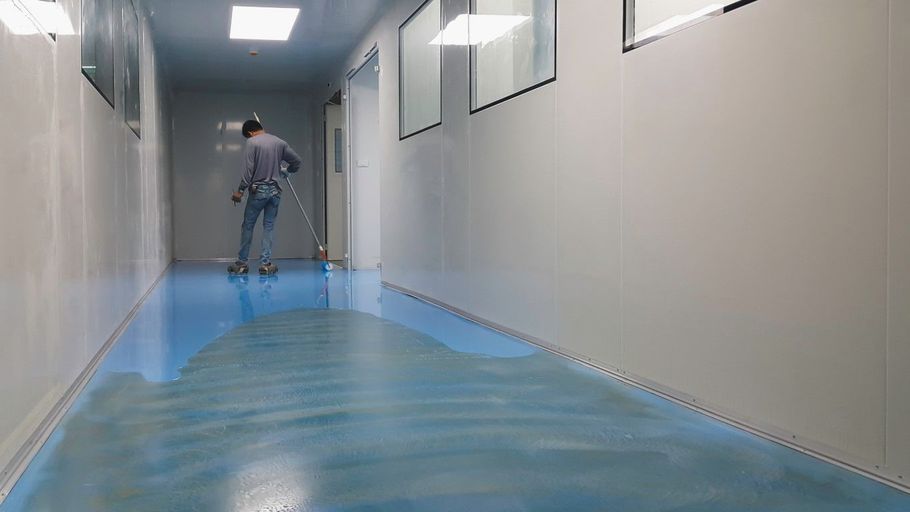 Worker applying blue epoxy coating to a commercial hallway floor