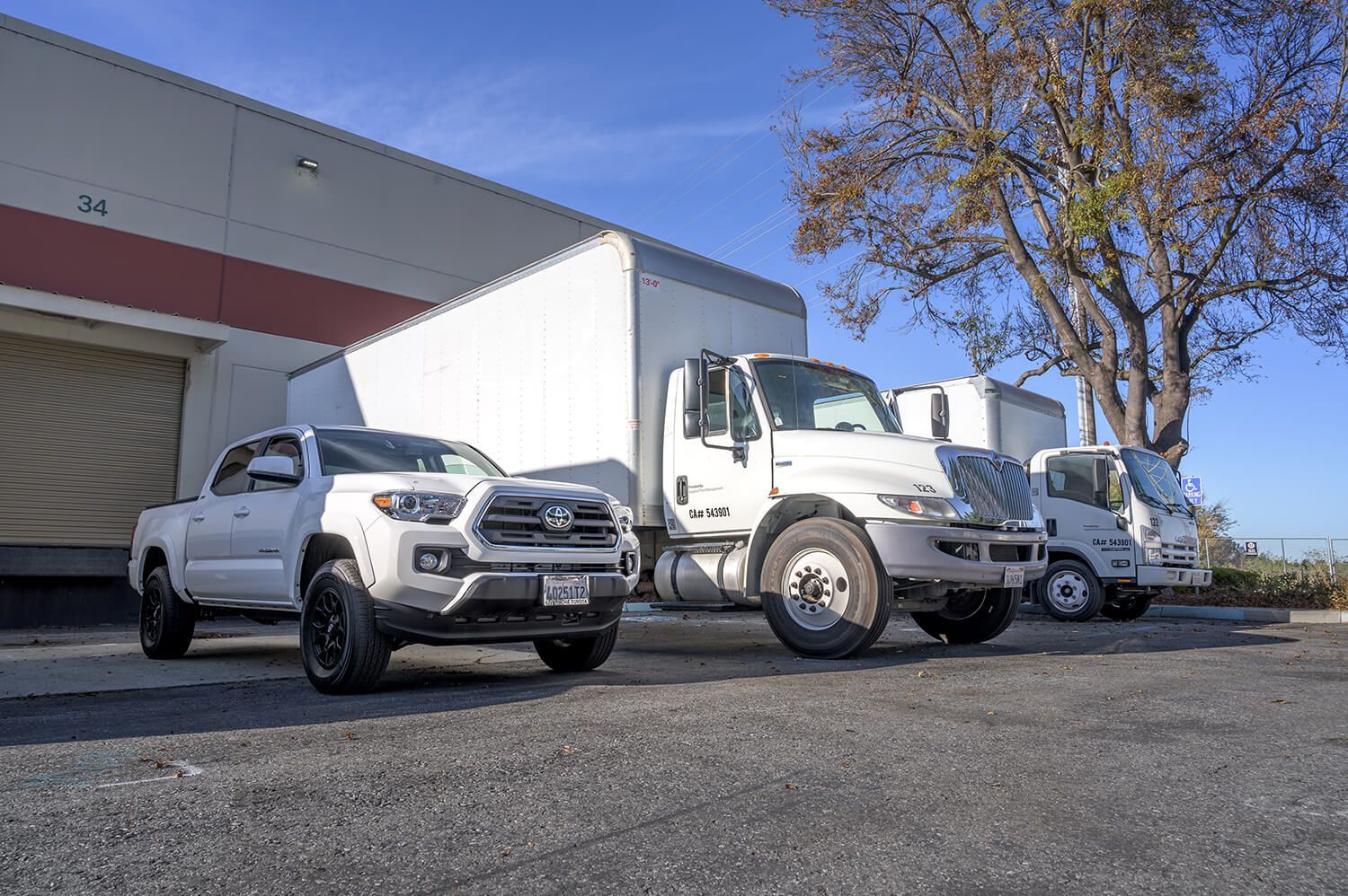 White pickup truck and two white semi trucks parked outside a warehouse on a sunny day | Adaptive Fleet Management