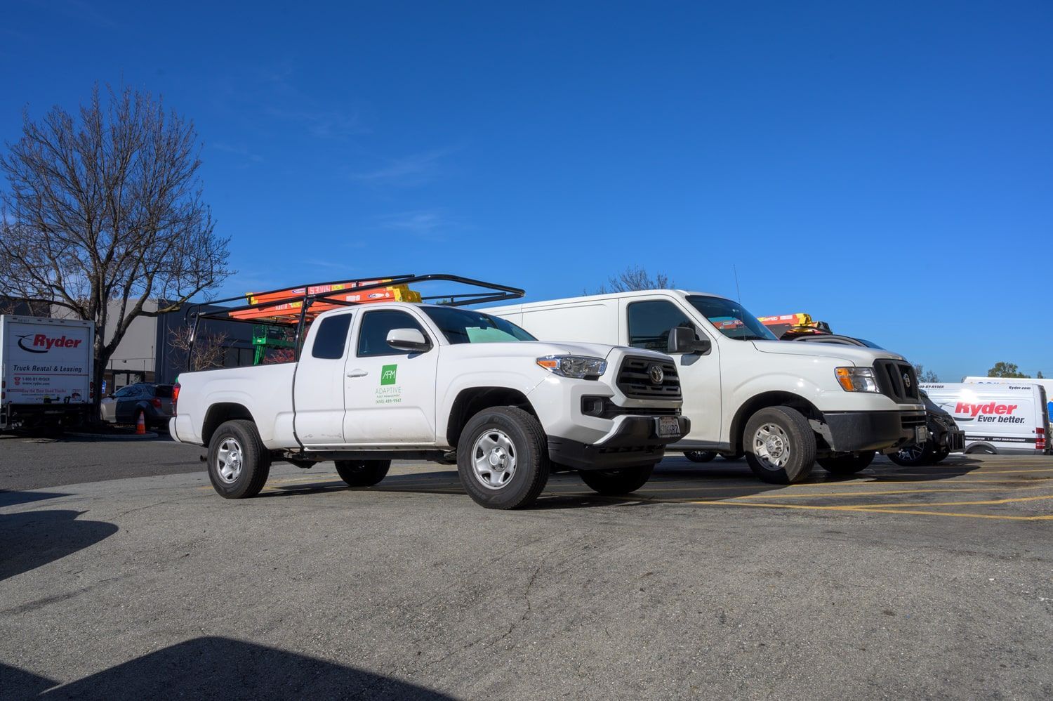 Two white pickup trucks parked outdoors on a gravel lot under a bright blue sky. | Adaptive Fleet Management