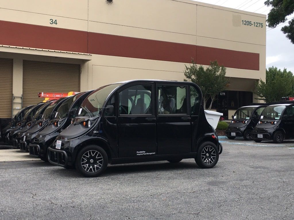 Black compact van parked outside a warehouse beside a row of similar vehicles. | Adaptive Fleet Management
