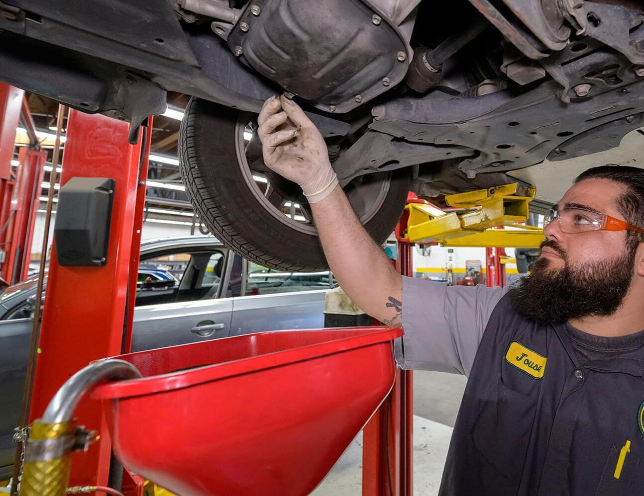 Mechanic inspecting a car’s underside in a repair shop, with a red drain pan below. | Adaptive Fleet Management