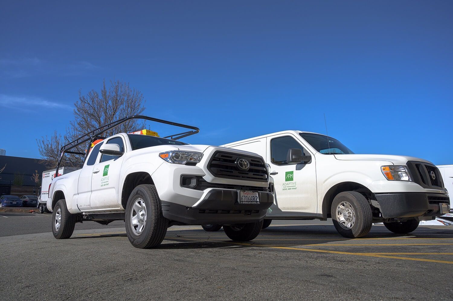 Two white utility trucks parked side by side under a clear blue sky | Adaptive Fleet Management