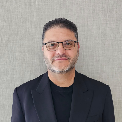 A man wearing glasses and a suit is standing in front of a wall.