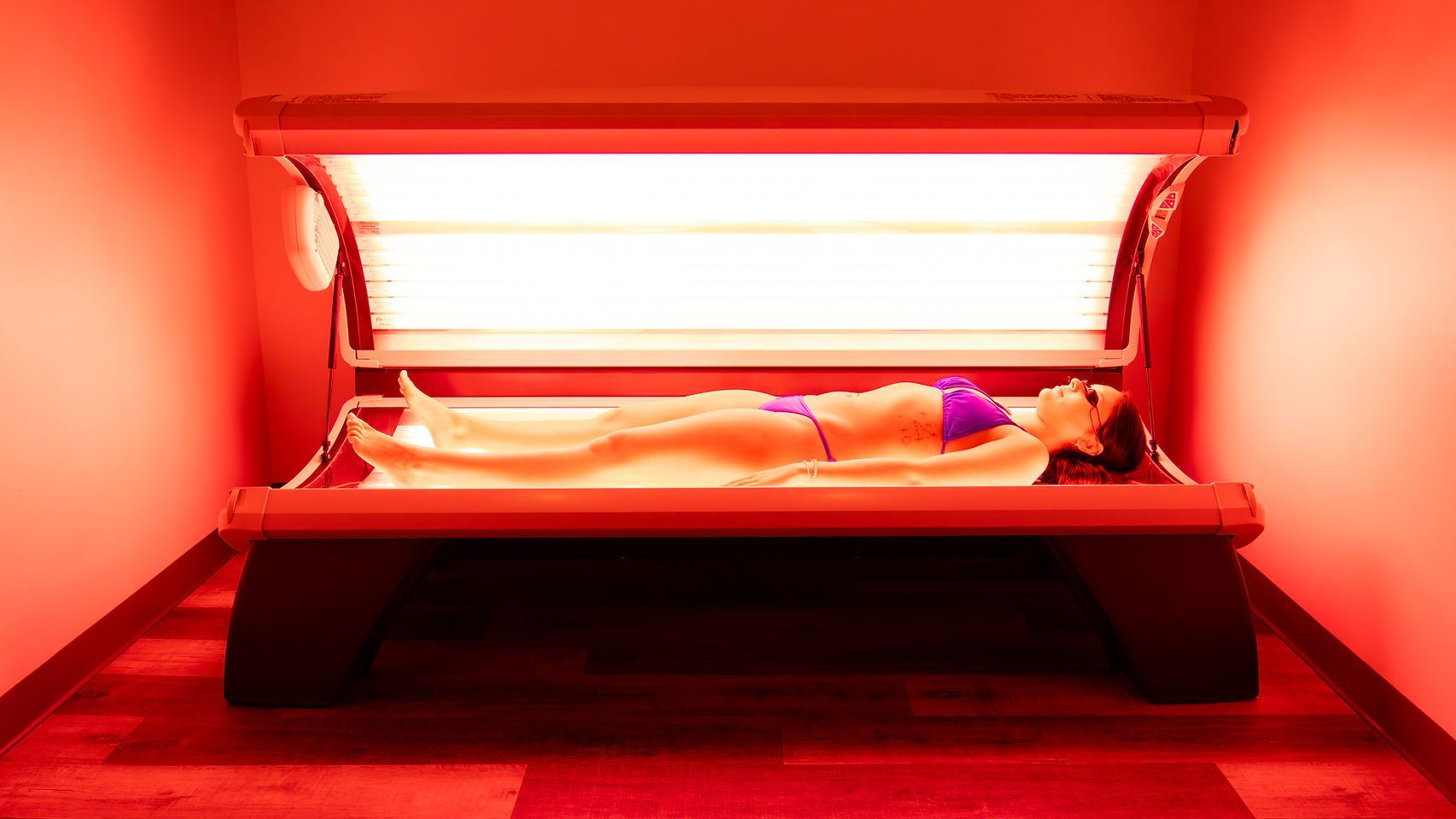 Person lying on a tanning bed under bright red light in a red-lit room
