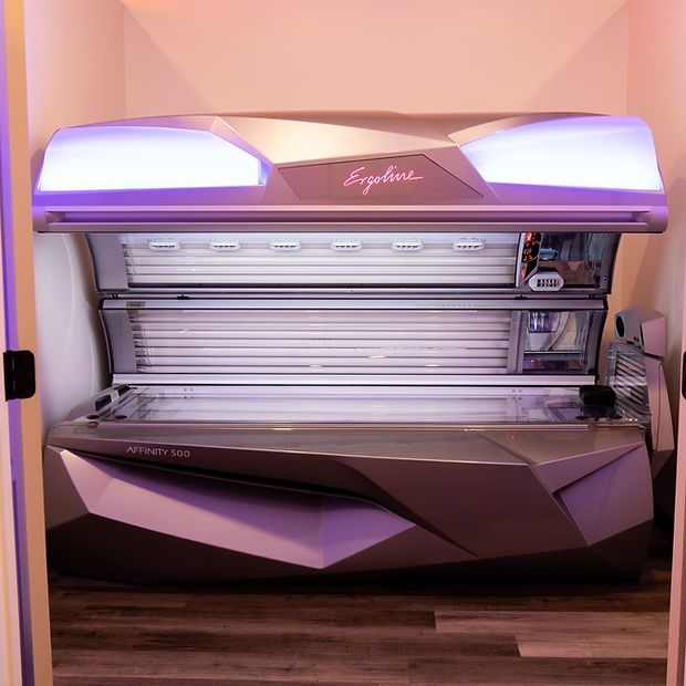 Purple tanning bed in a salon room with pink walls and wood flooring