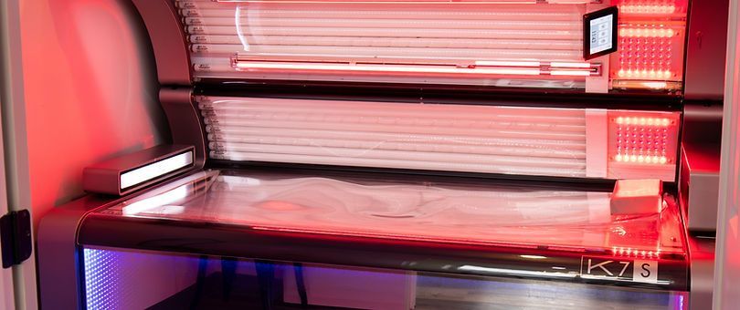 Indoor tanning bed with pink and red LED lights in a dark room