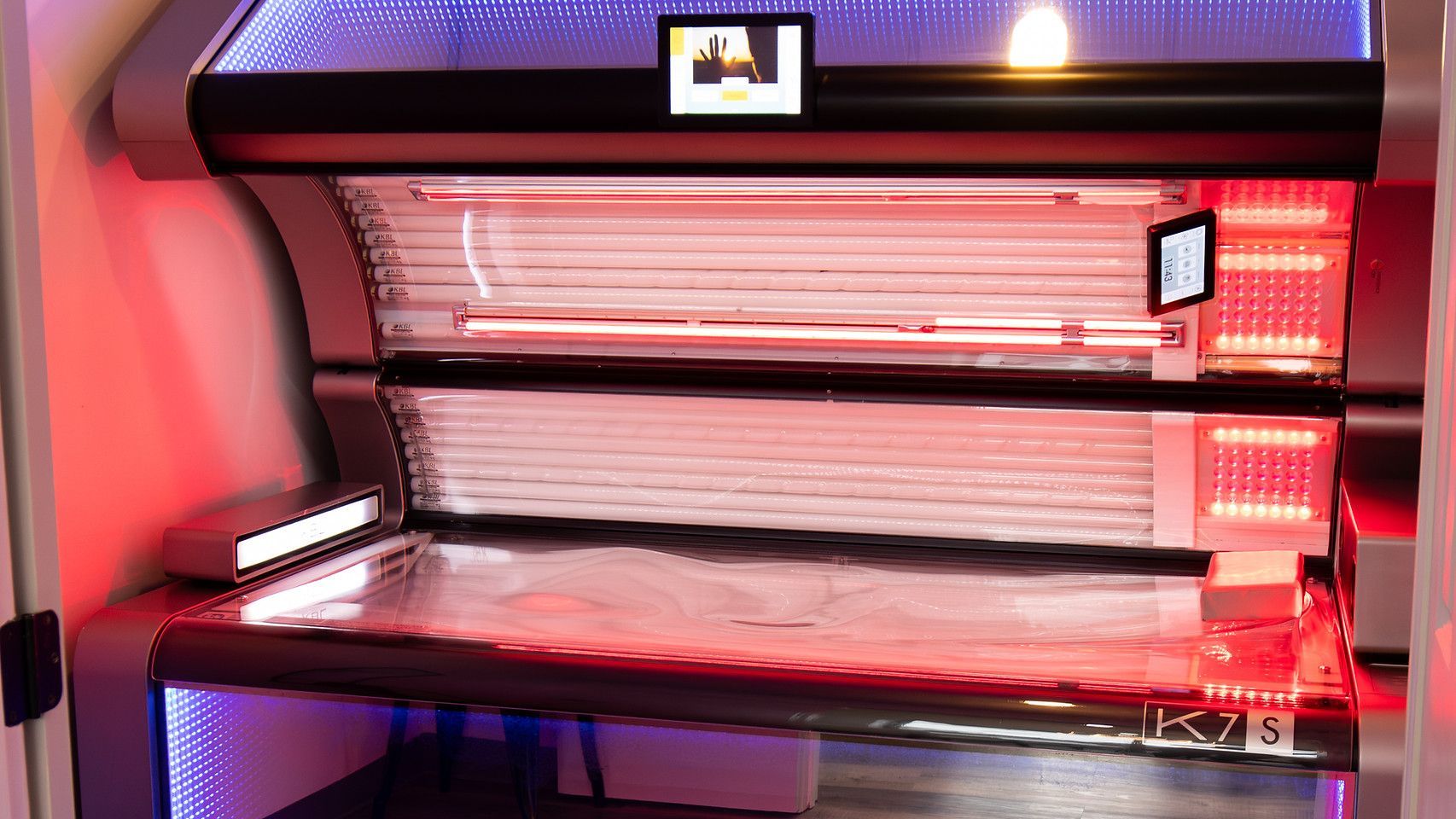 Red-lit tanning bed with open lid and glowing interior panels