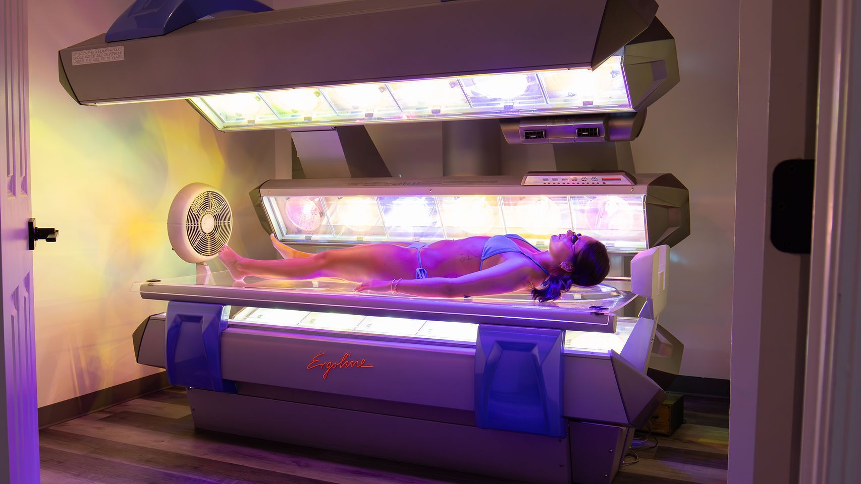 Three people tanning in a glowing multi-level tanning bed booth