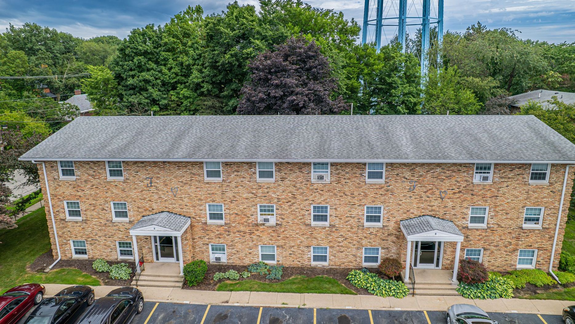 Two-story apartment building with stone facade; parked cars in front, water tower in the background.