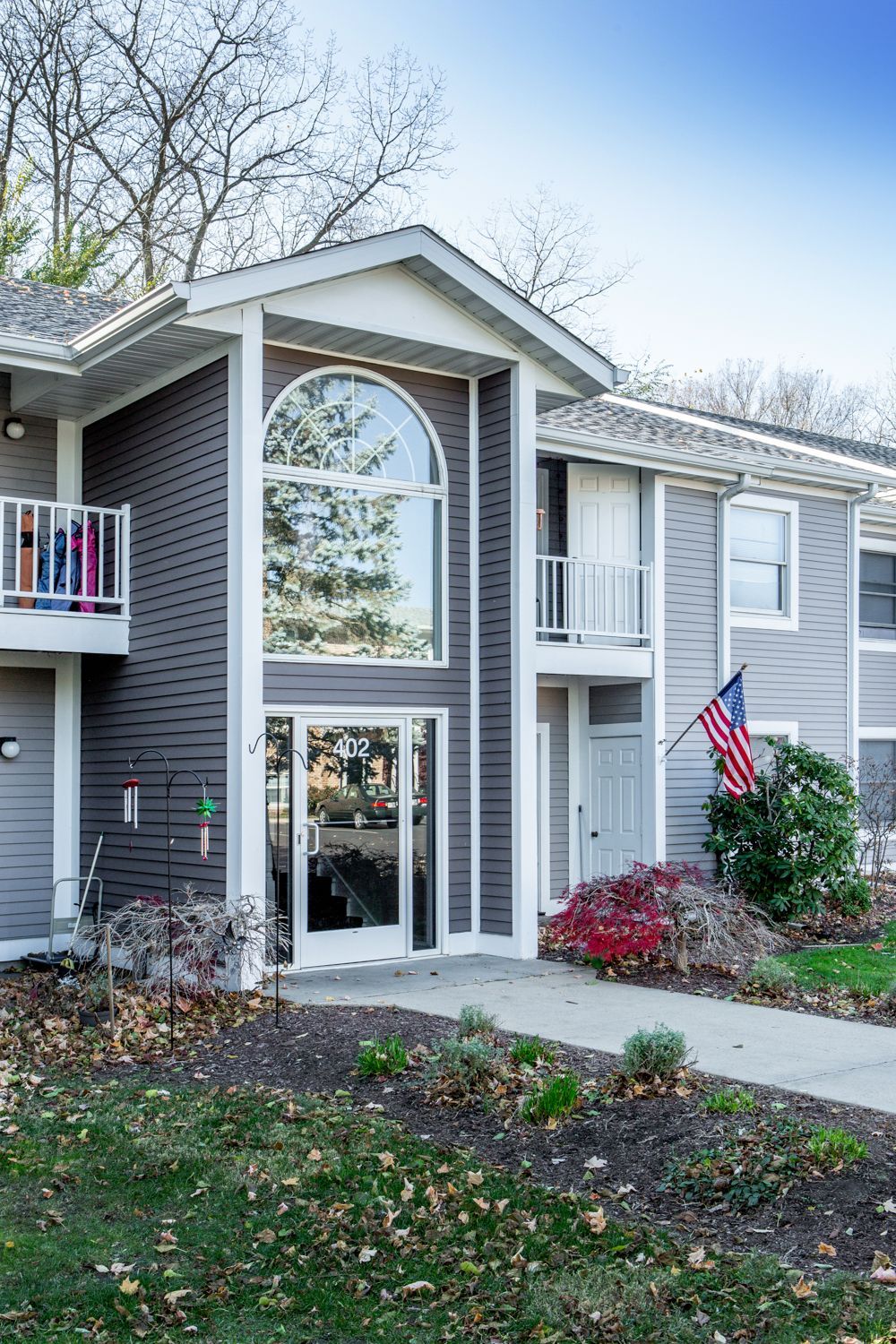 Two-story gray apartment building with large arched window and US flag.