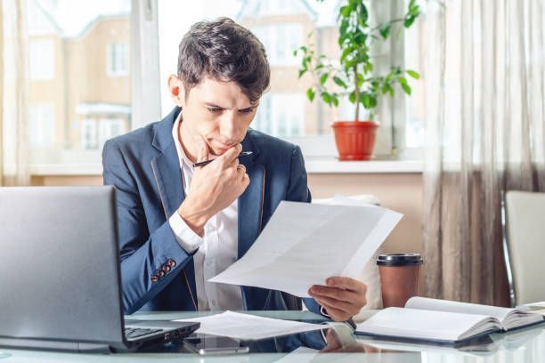 A man is sitting at a desk with a laptop and a piece of paper.