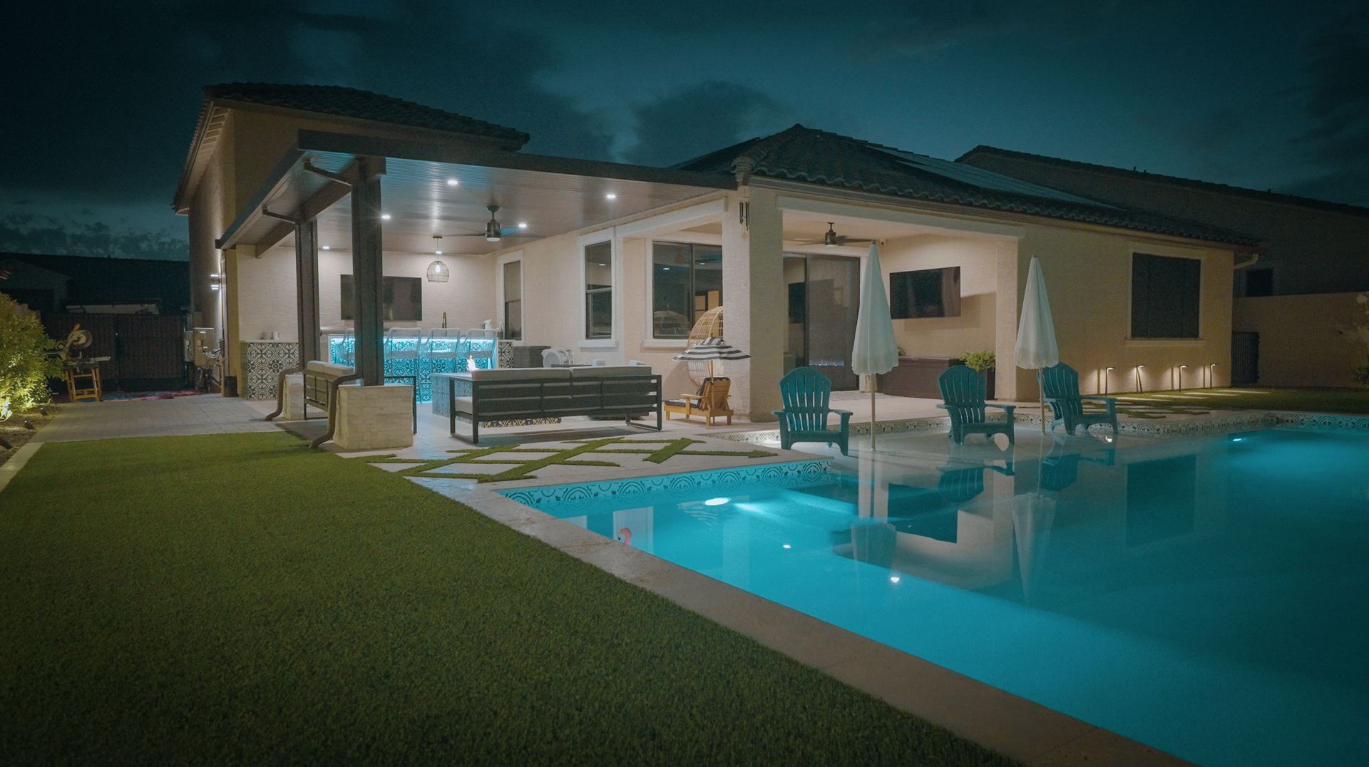 A house with a large swimming pool in the backyard at night.
