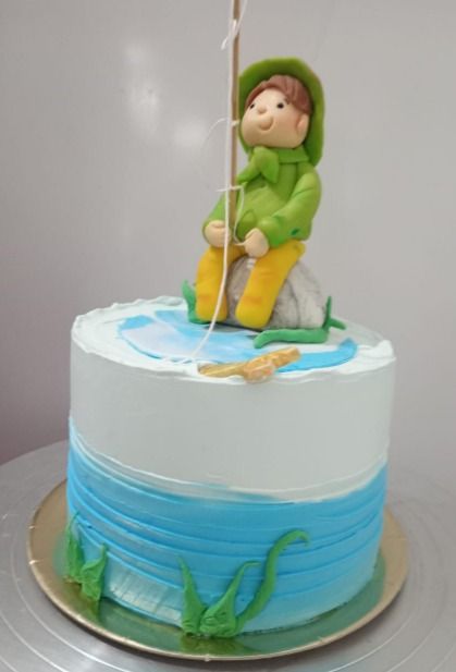 Pastel decorado con figura de pescador, glaseado azul y blanco y detalles de agua.