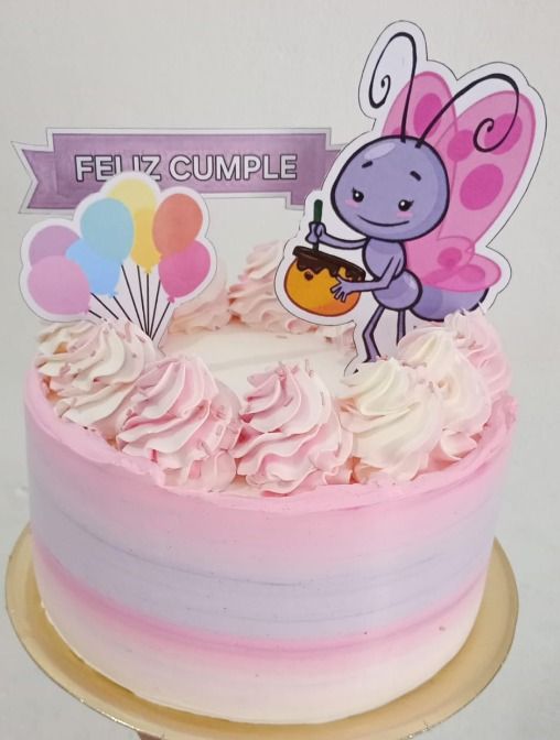Pastel con glaseado rosa y morado, decoración de mariposas, globos y pancarta de “Feliz Cumpleaños”.