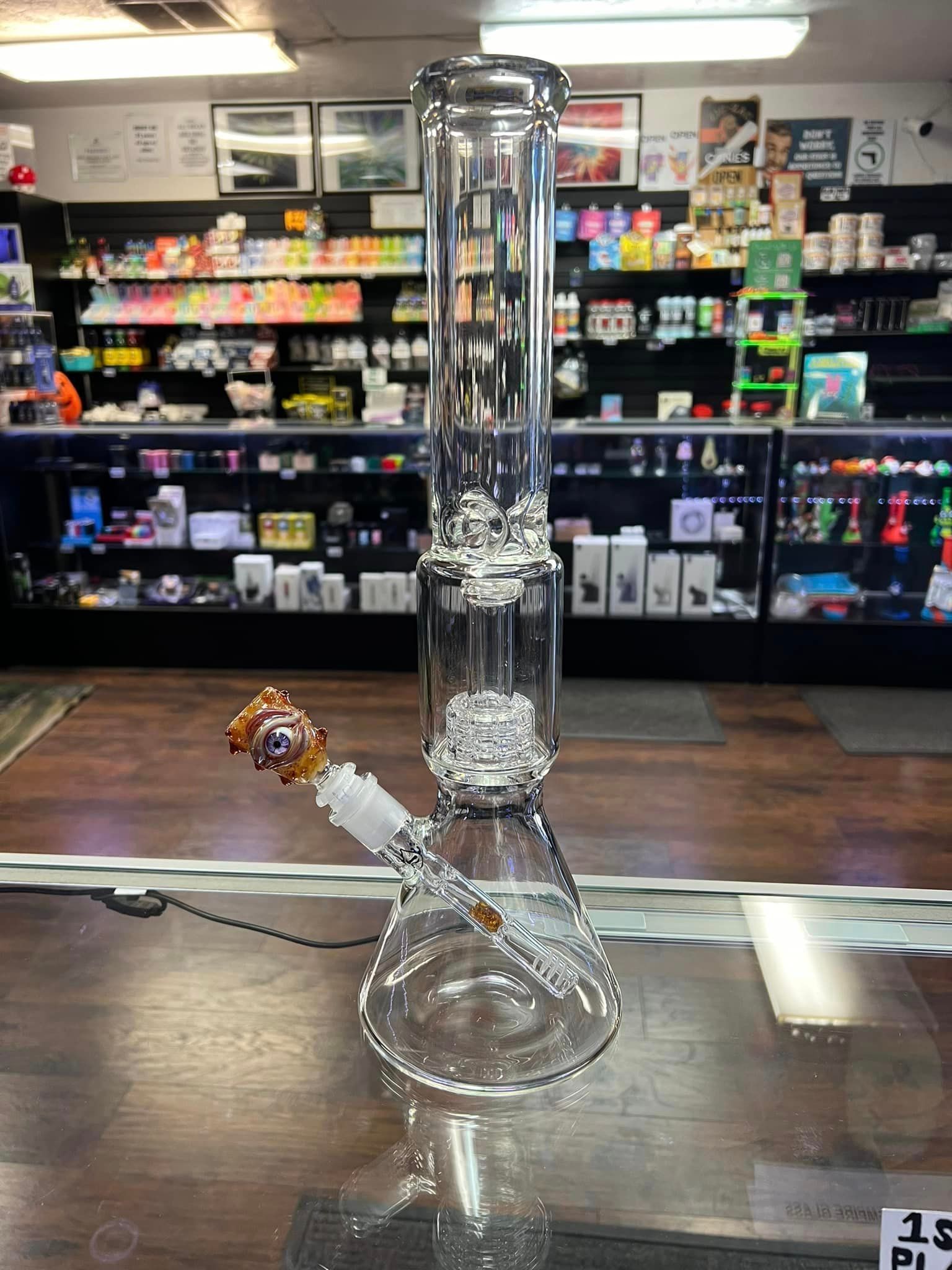 A clear glass bong is sitting on a glass table in a store.