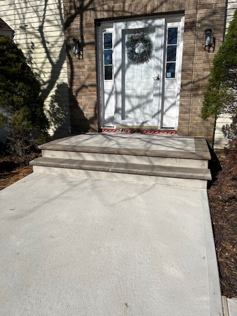 A concrete walkway leading to a white door with a wreath on it.