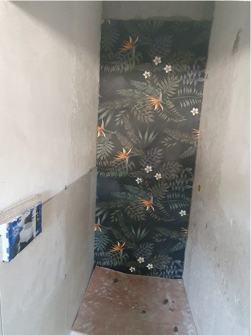 Carta da parati con motivo di foglie e fiori tropicali su una parete parzialmente costruita.