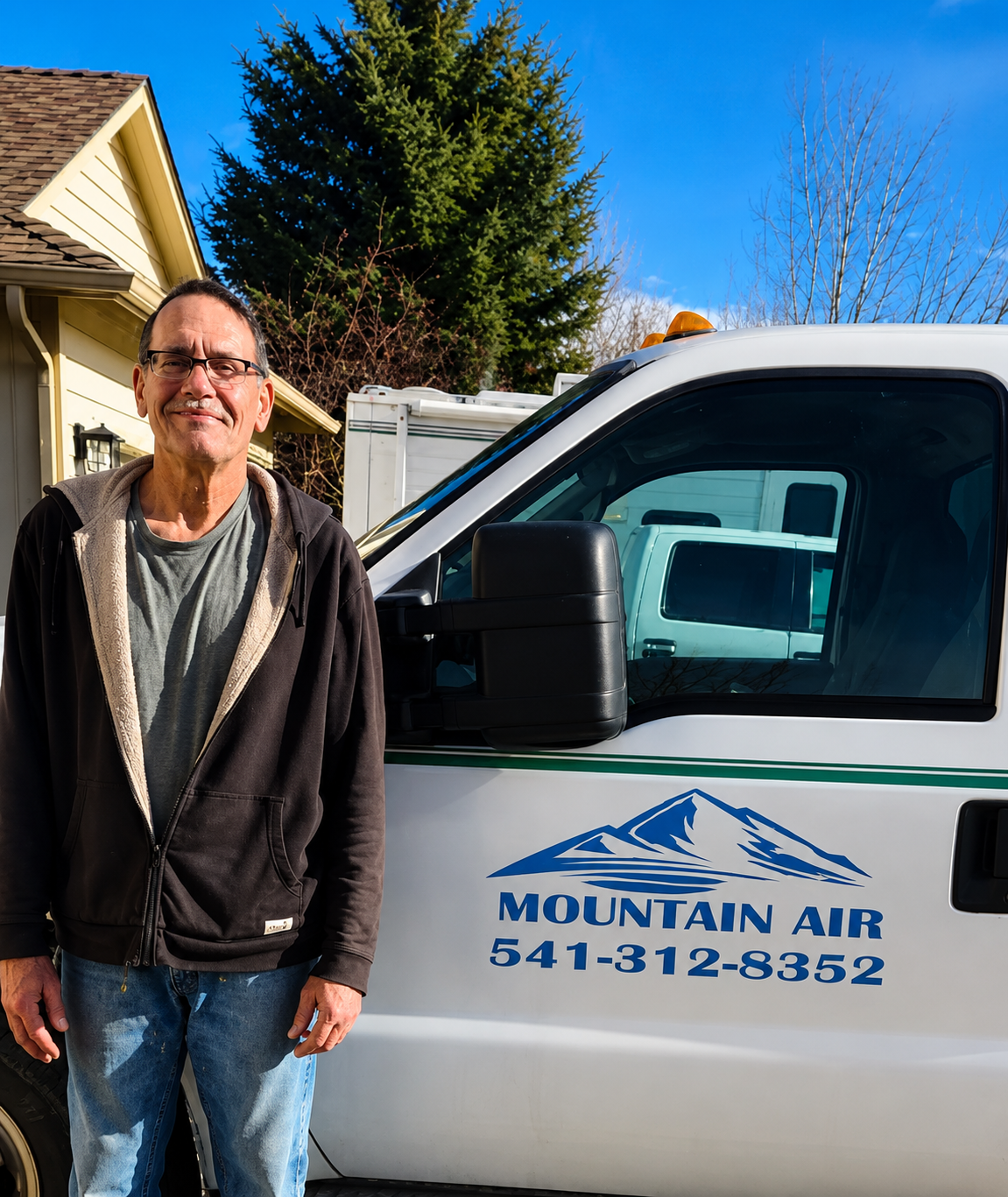 Man standing beside a white Mountain Air service van on a sunny suburban driveway