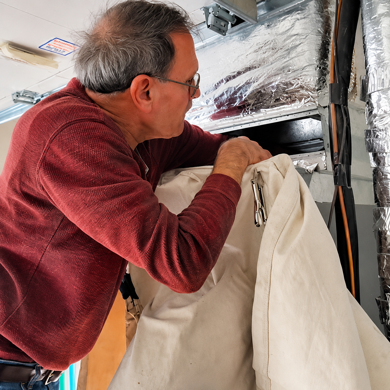 Man in red sweater inspecting insulation inside a wall cavity