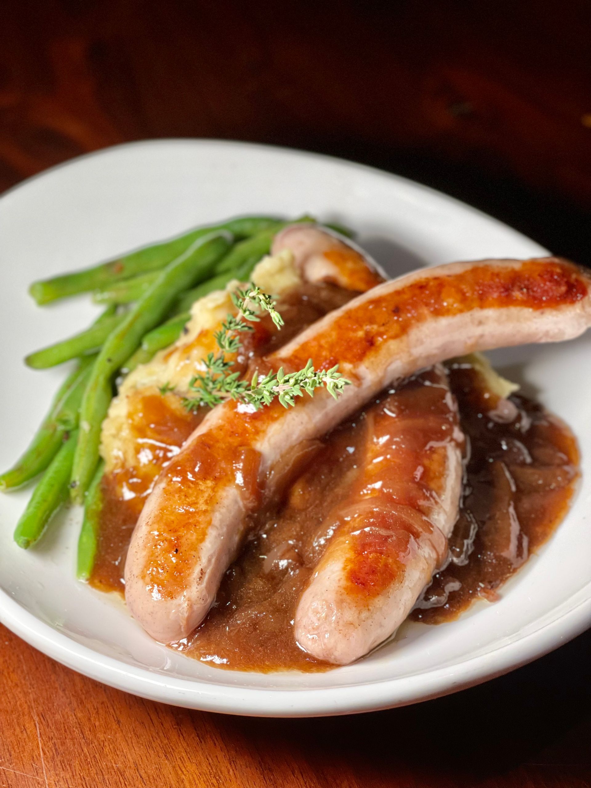 A white plate topped with sausages , mashed potatoes and green beans.