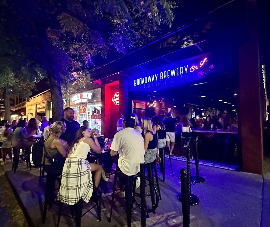 A group of people are sitting at tables outside of a brewery at night.