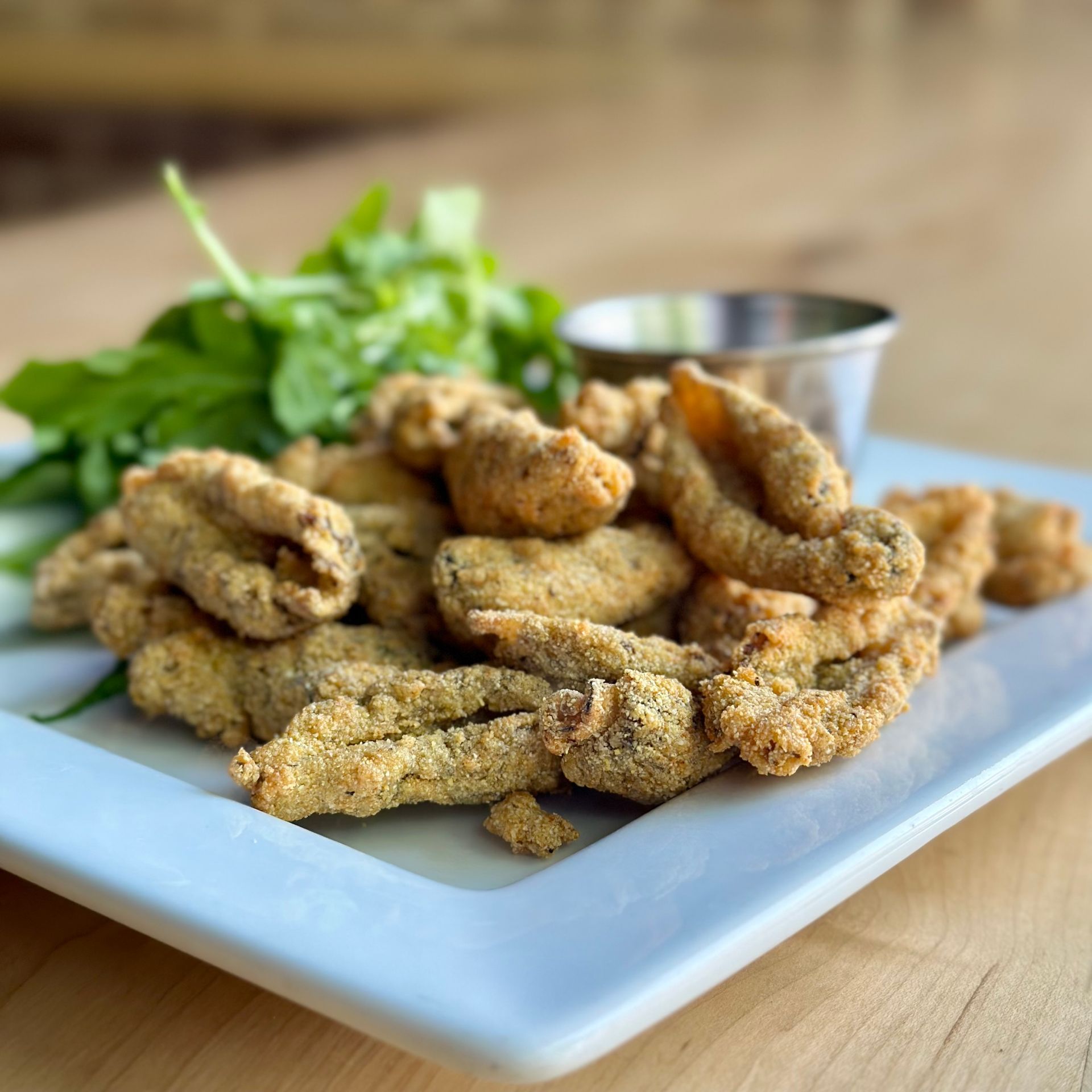 A white plate topped with fried morel mushrooms and greens on a wooden table.