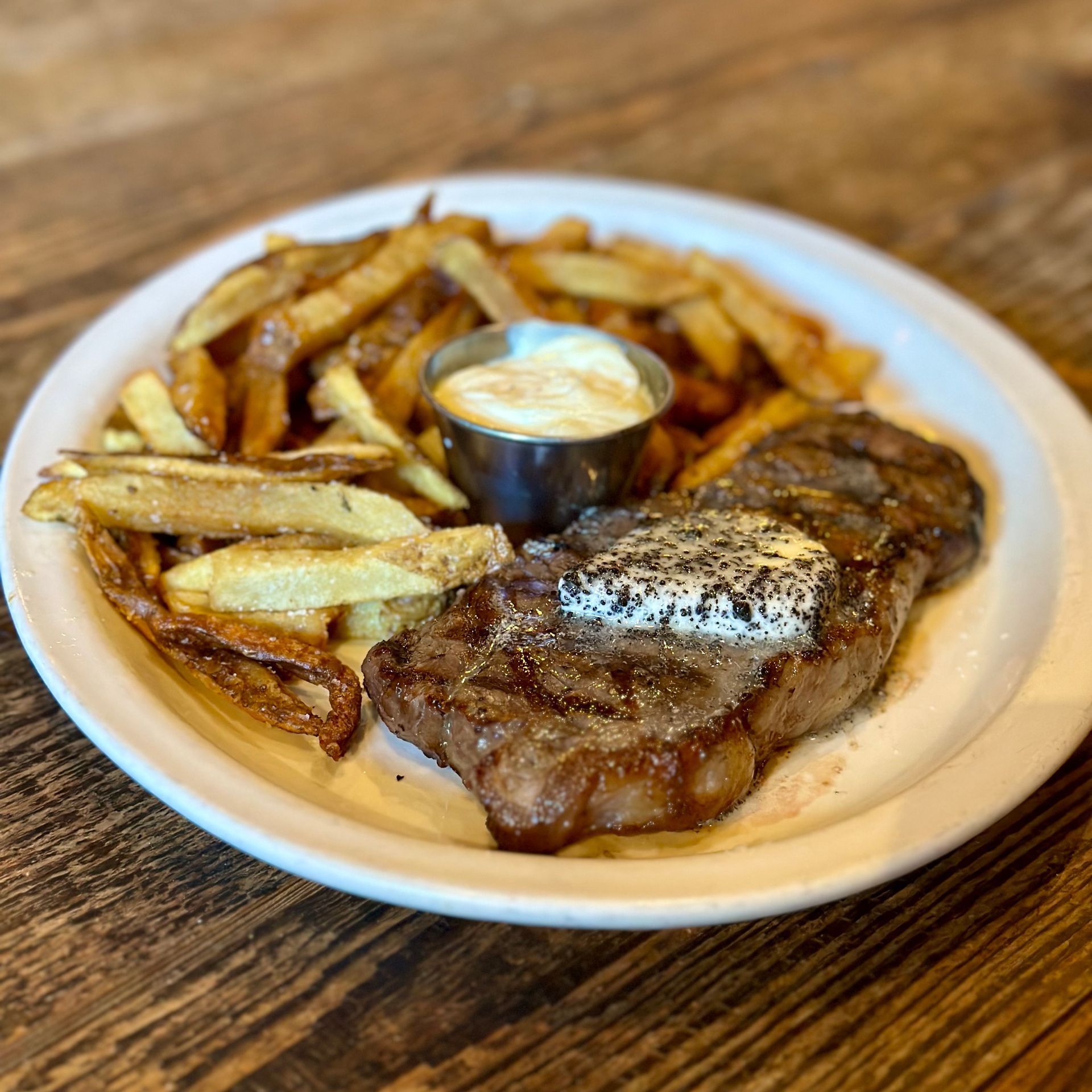 A white plate topped with a steak and french fries on a wooden table.