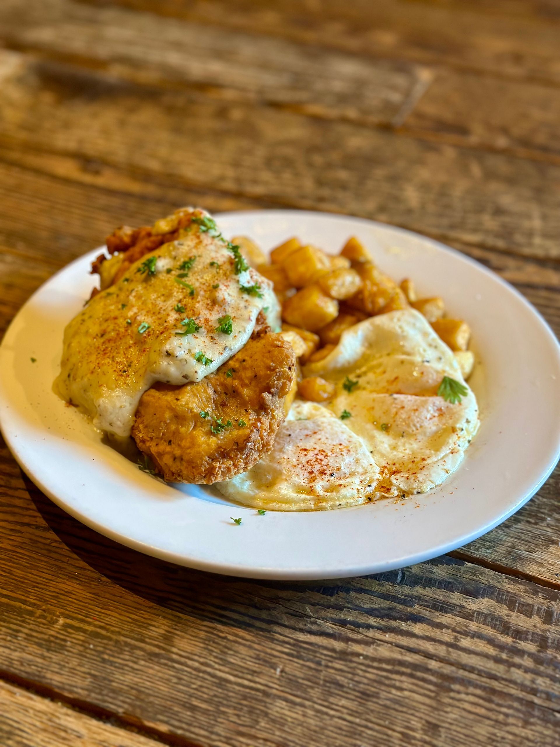 A plate of food with eggs, fried chicken, and potatoes on a wooden table.