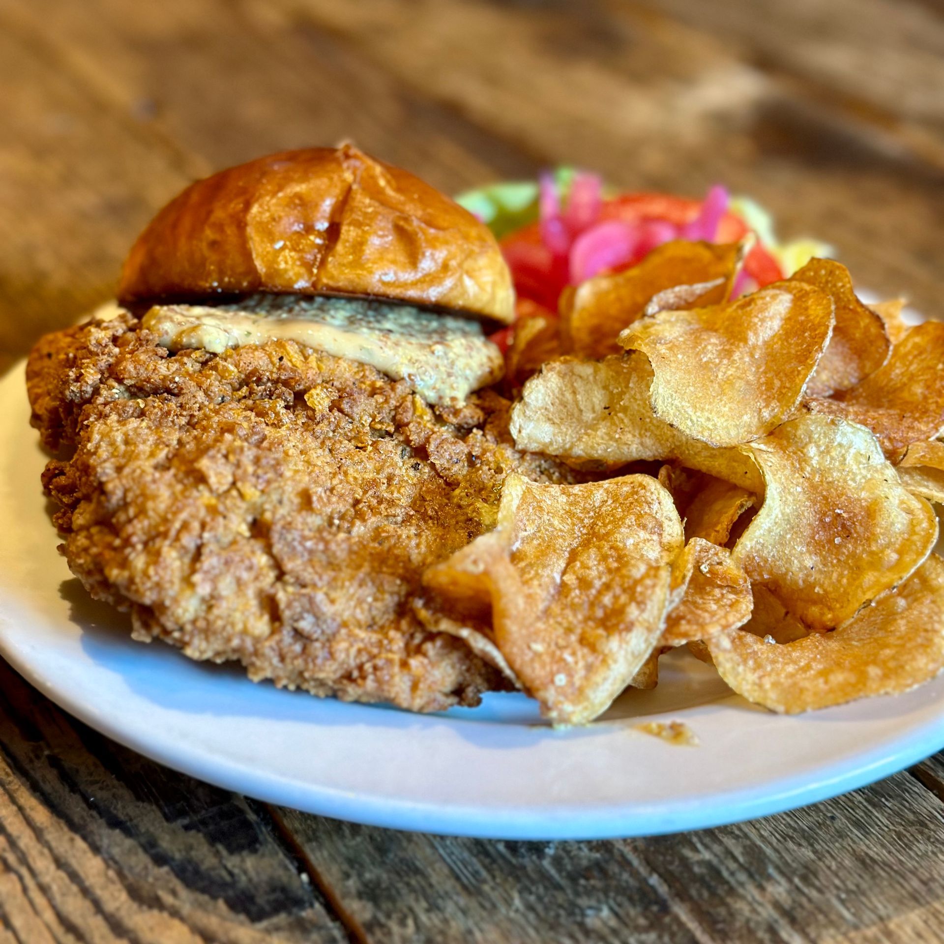A plate of food with a chicken sandwich and potato chips on a wooden table.