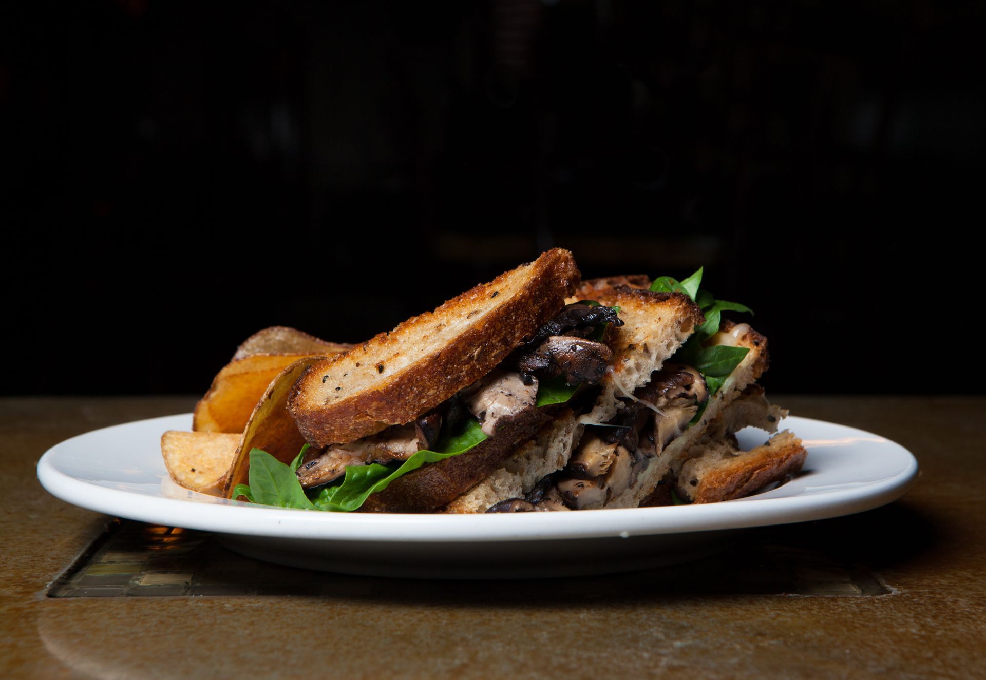 A close up of a sandwich on a plate with potatoes.