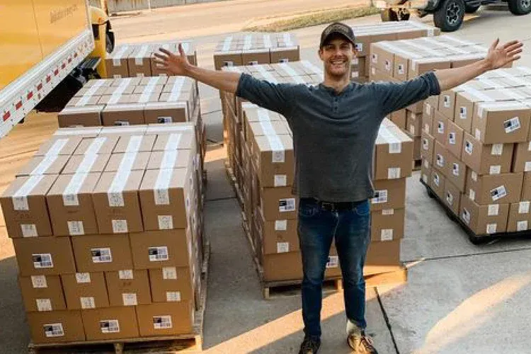A man is standing in front of a truck full of boxes.