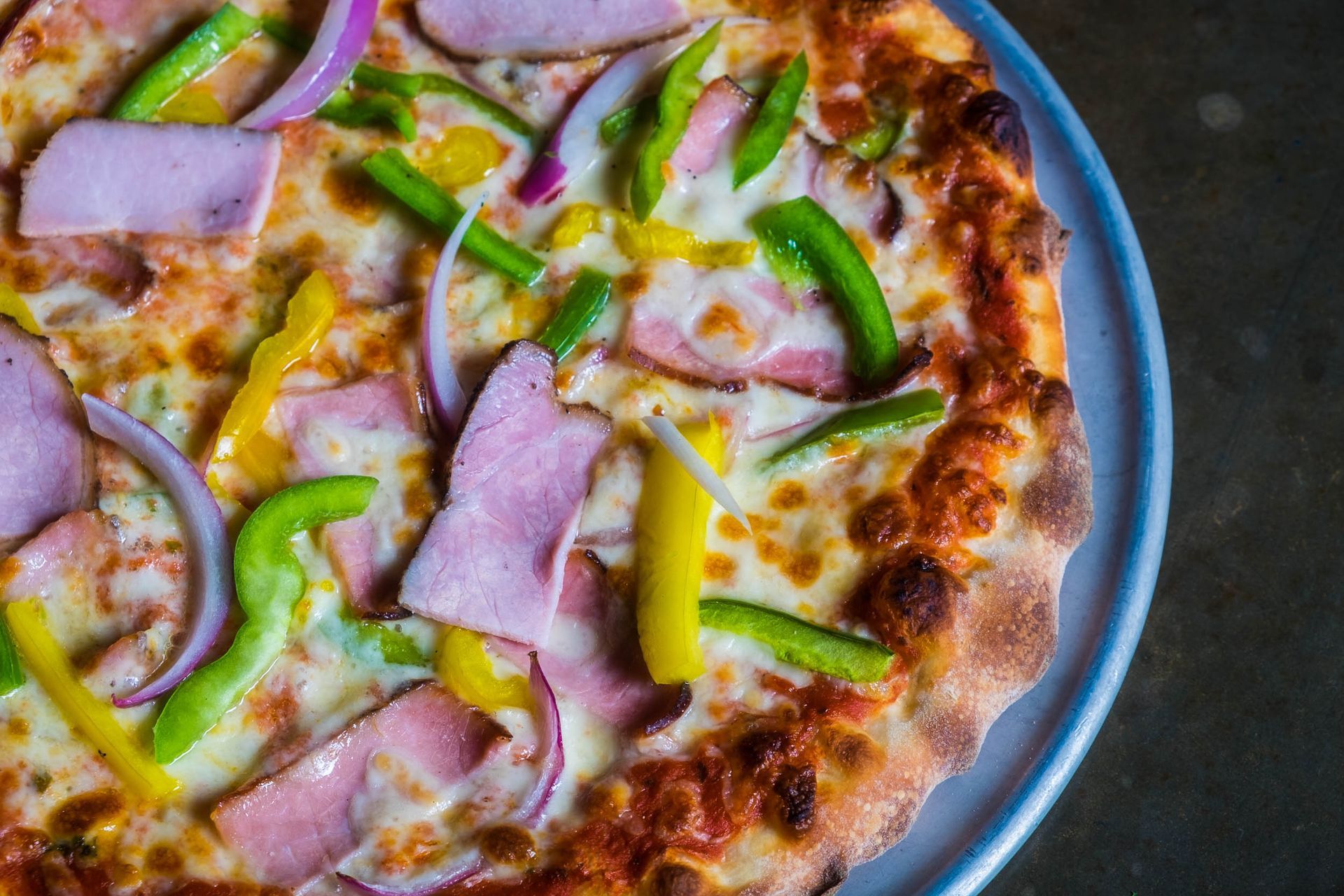 A pizza with ham , peppers , onions and cheese on a plate.