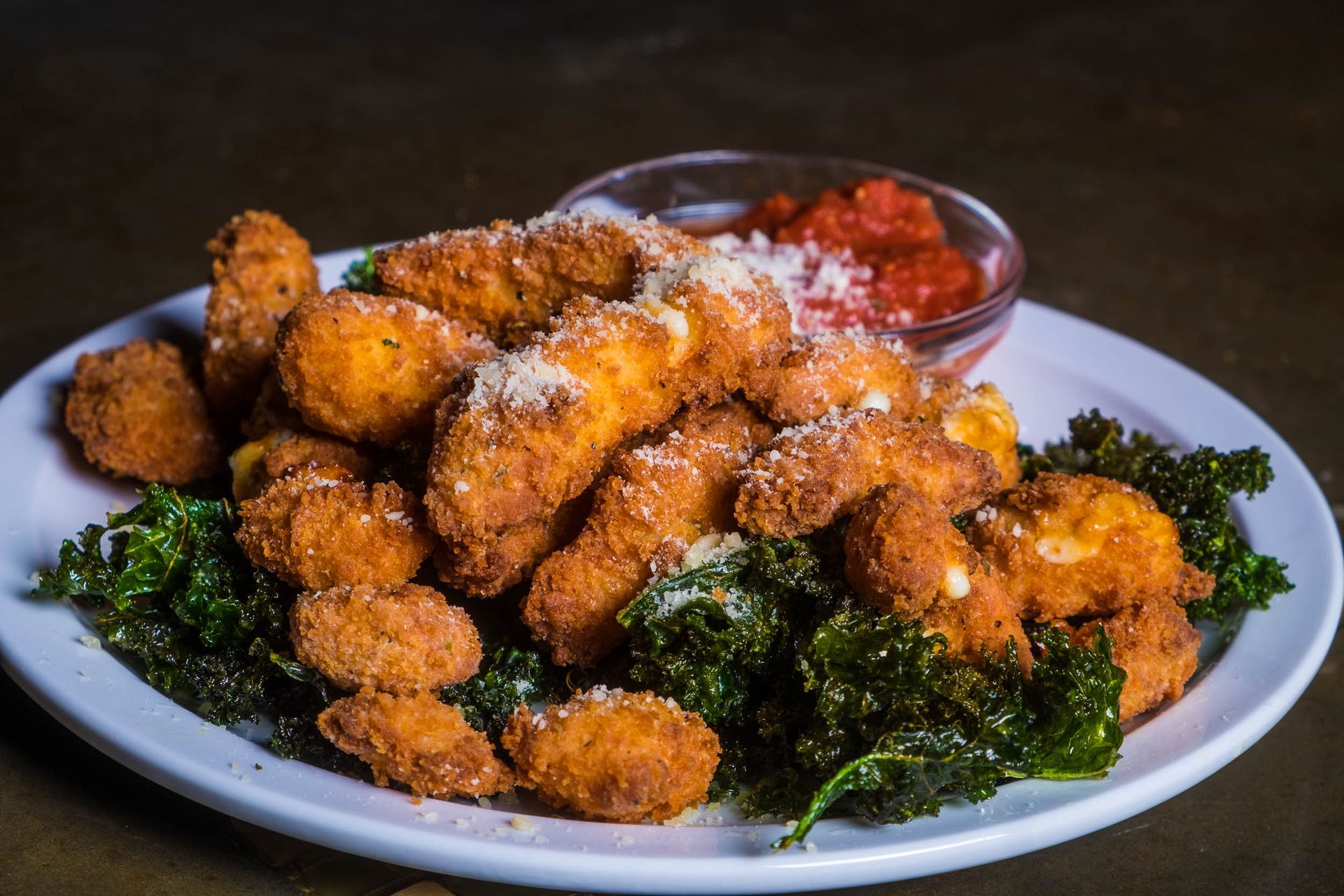 A white plate topped with fried cheese curds and kale.