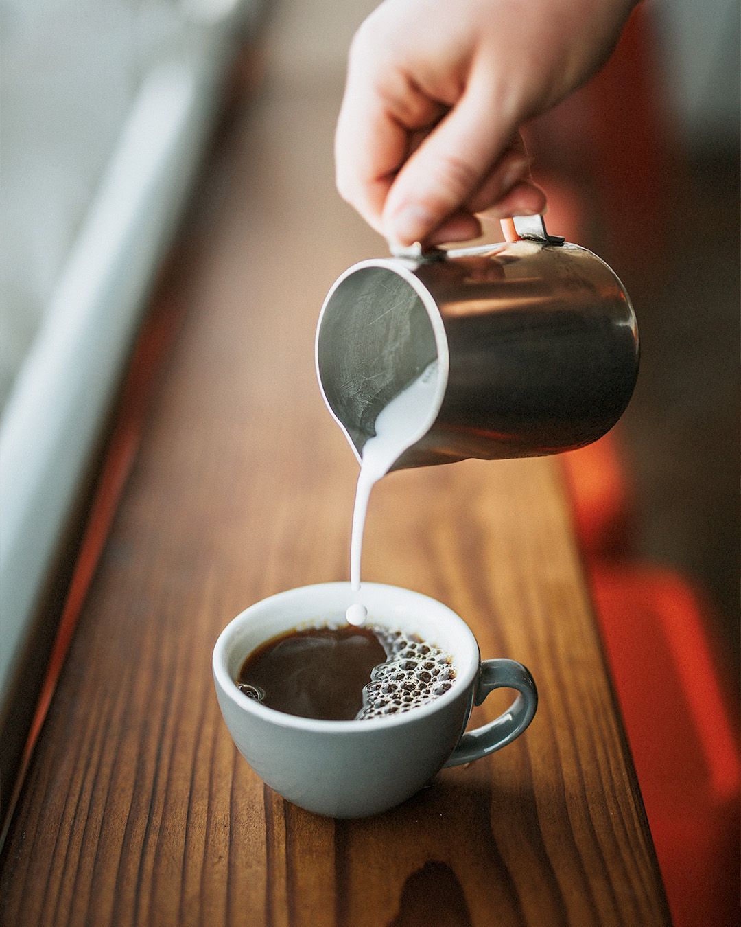 A person is pouring milk into a cup of coffee