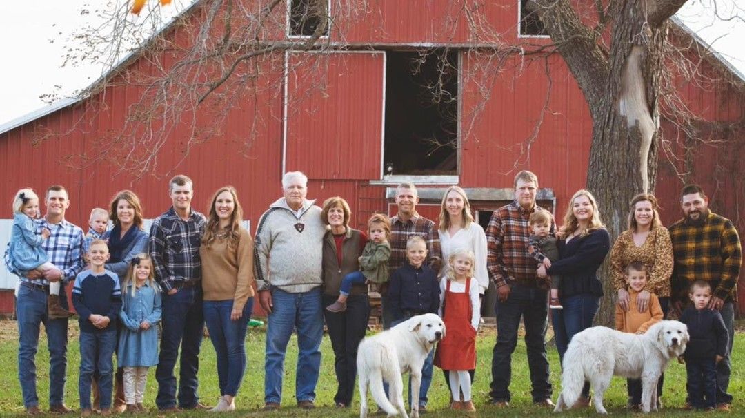 A large family is posing for a picture in front of a red barn.