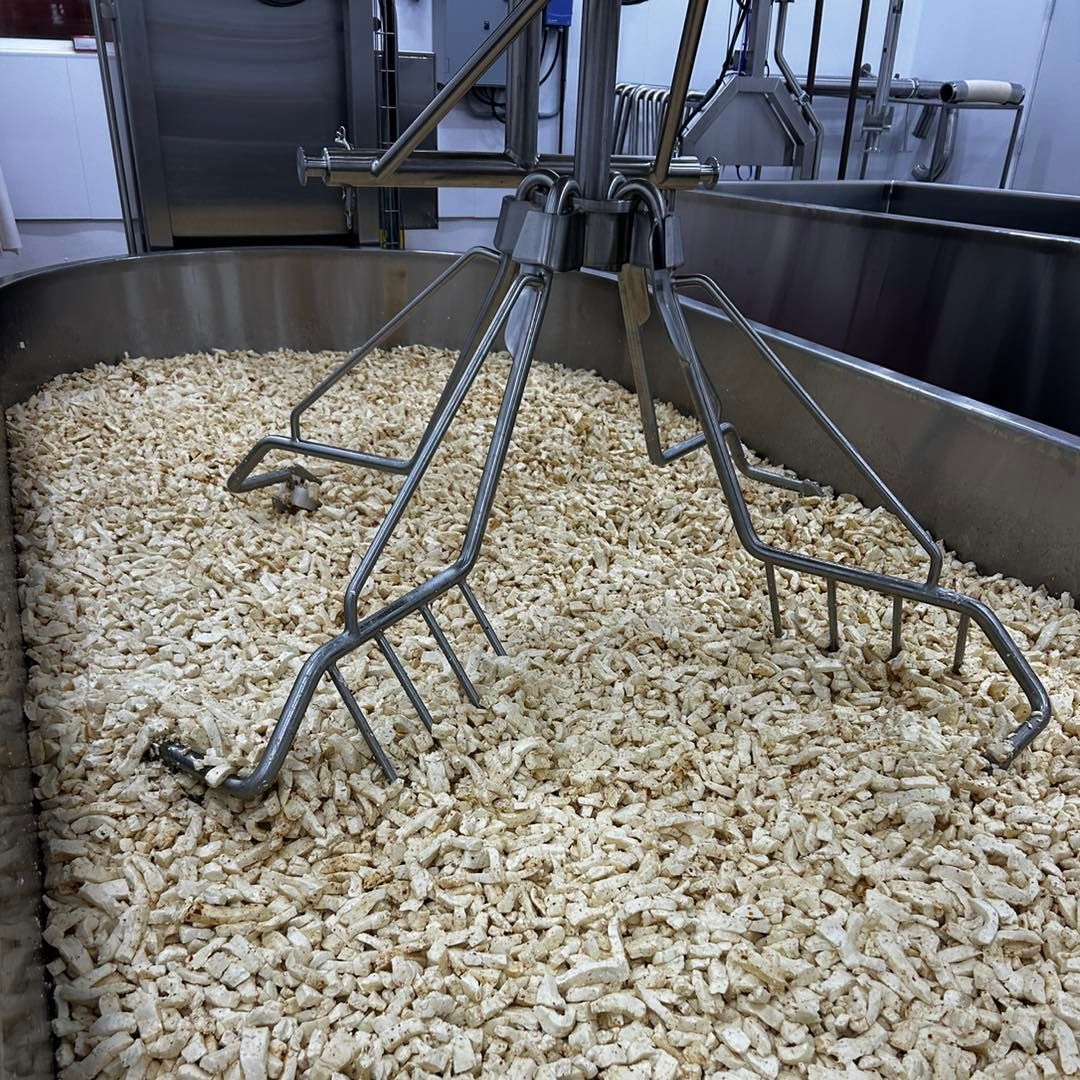 A large metal container filled with cheese curds and whey