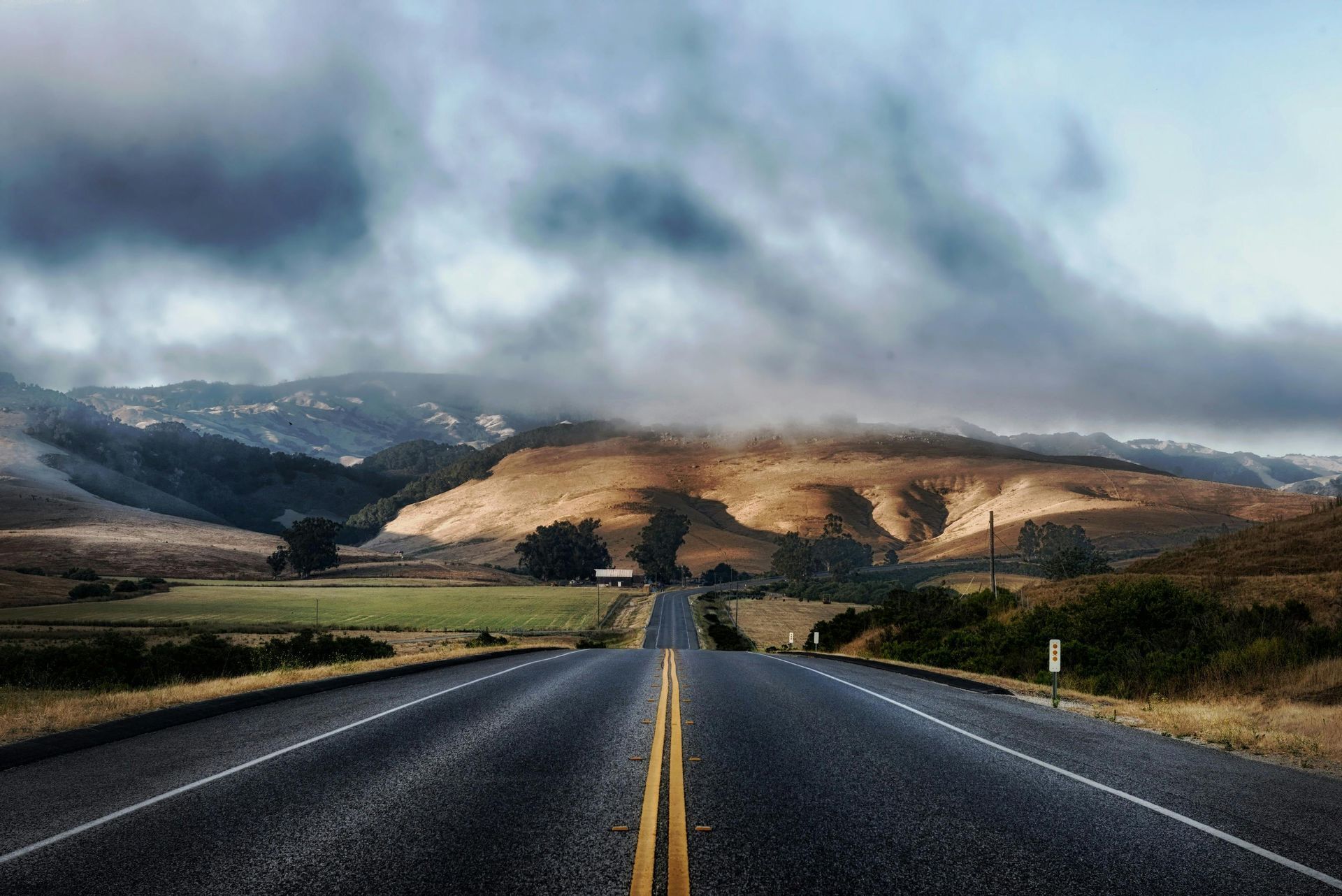 Open road leading into misty hills under dramatic clouds