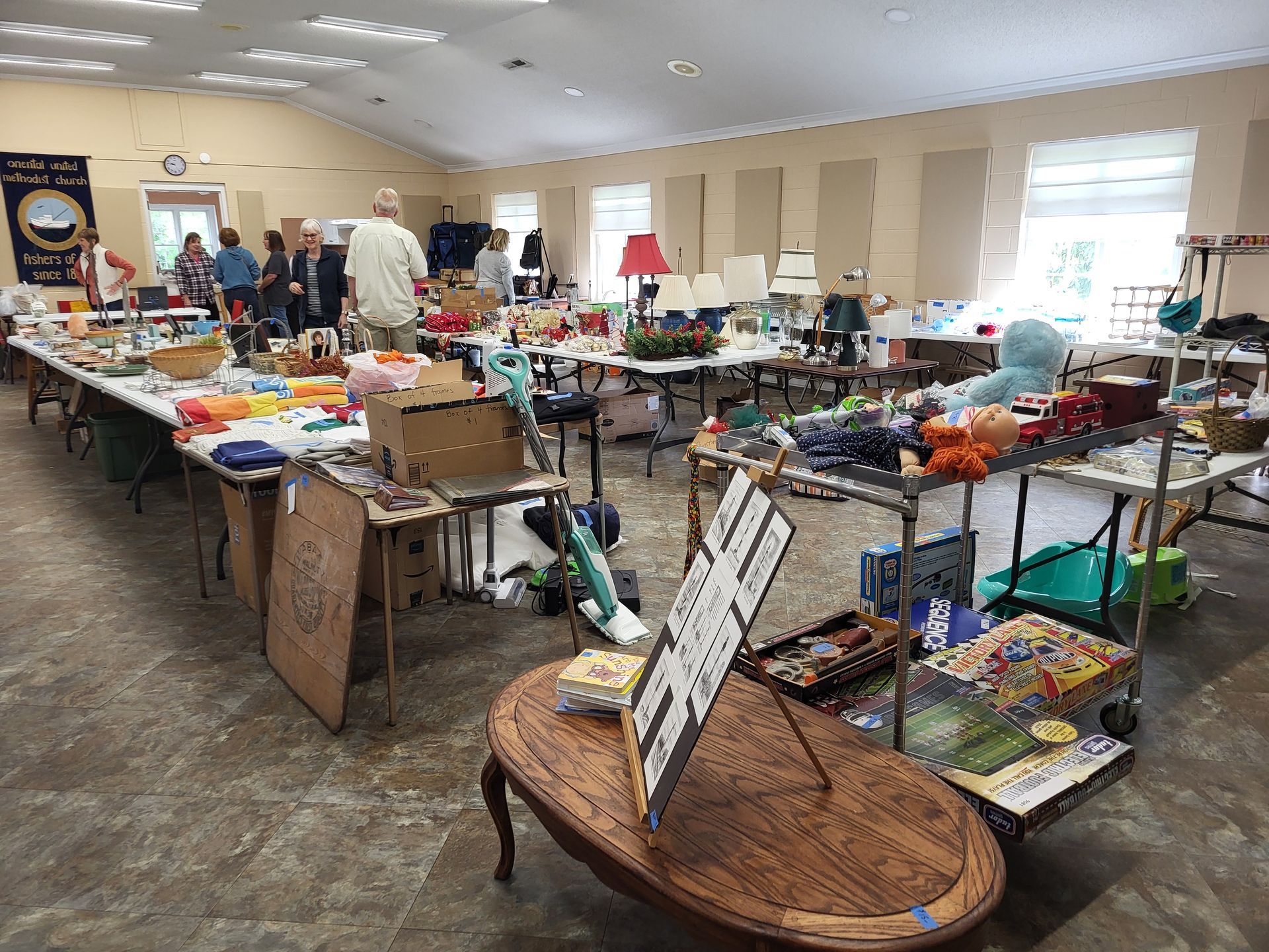 Craft fair with vendors and shoppers browsing tables filled with goods inside a large hall.
